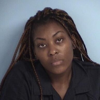 Mug shot of black woman with long hair wearing a blue jumpsuit