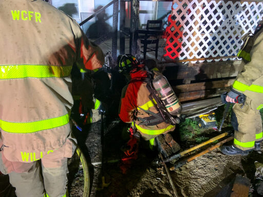 Firefighters working under the burnt front porch of a mobile home