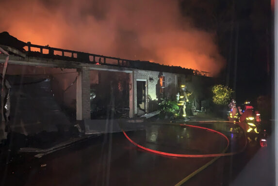 Firefighters extinguishing a fire at the back of a brick home in the dark