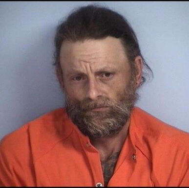White male with dark brown hair and brown/gray beard in orange jumpsuit