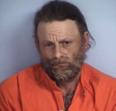 White male with dark brown hair and brown/gray beard in orange jumpsuit