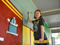 Mrs. Dotson smiles from a ladder as she paints the mural