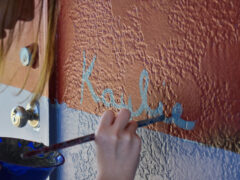 Artist painting her name "Kaylie" on her mural