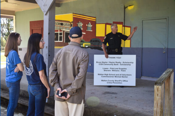Deputy standing with a thank you sign pointing at a mural