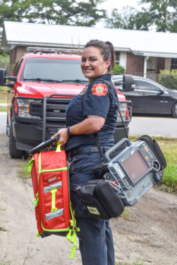 A paramedic stands with a medical bag and monitor