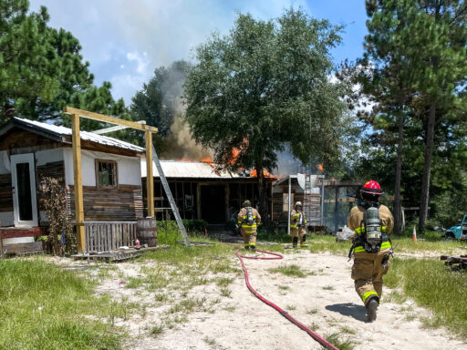 Firefighters in bunker gear running towards a home on fire