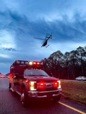 Photo of an ambulance and helicopter hovering over it.