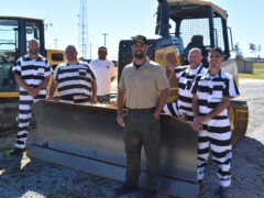 Inmates and their instructor pose in front of a front end loader