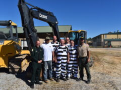 Inmates pose with their vocational instructor next to a backhoe