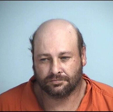 White balding man with a brown beard wearing an orange jumpsuit