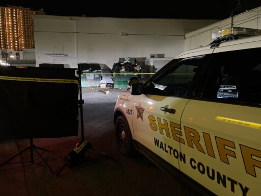 A Walton County Sheriff's Office car parked in front of dumpsters with crime scene tape.