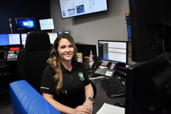 Photo of a dispatcher sitting down at a console smiling.