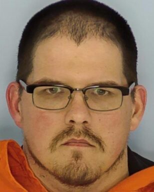 Mug shot of a white male with glasses and dark colored hair and brown goatee.