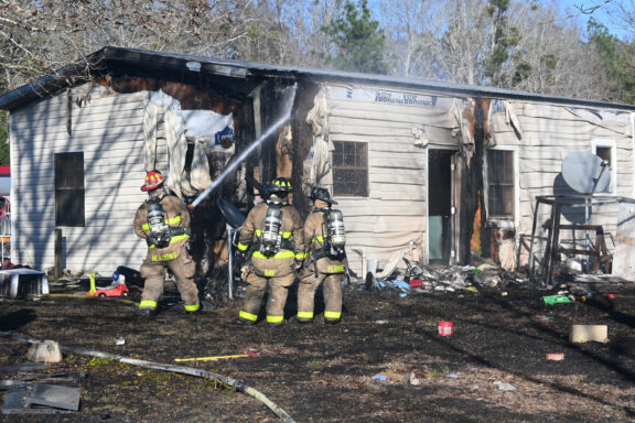 Three firefighters standing outside of a fire damaged single-story home