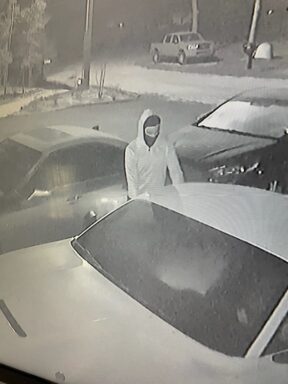 Black male with a ski mask stands at the passenger side of a vehicle