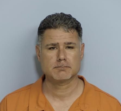 Mug shot of a man with black and gray hair wearing an orange jumpsuit