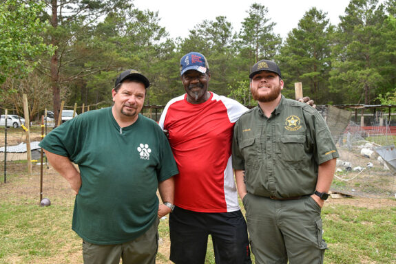 Two white male animal control officers wearing dark green standing with an elderly black male