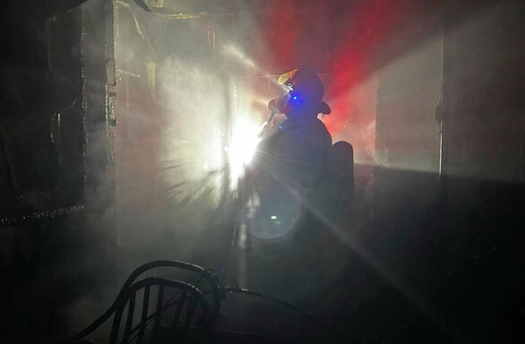 Firefighter standing in dark, fire damaged home with a flashlight on helmet