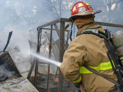 Firefighter wearing red helmet spraying water on a barn that is on fire