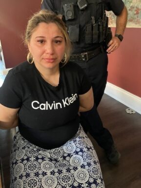 female wearing a Calvin Klein shirt handcuffed with an officer standing behind her.