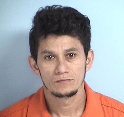 Mug shot of a Hispanic male with black hair wearing an orange jumpsuit in front of a blue wall.