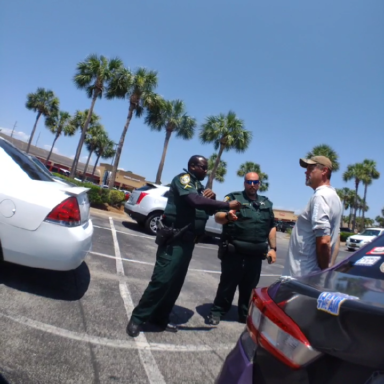 Two deputies standing in front of a white male in handcuffs with palm trees in the back ground.