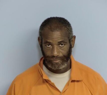 Mug shot of a black male wearing an orange jumpsuit with a black and gray peppered beard.