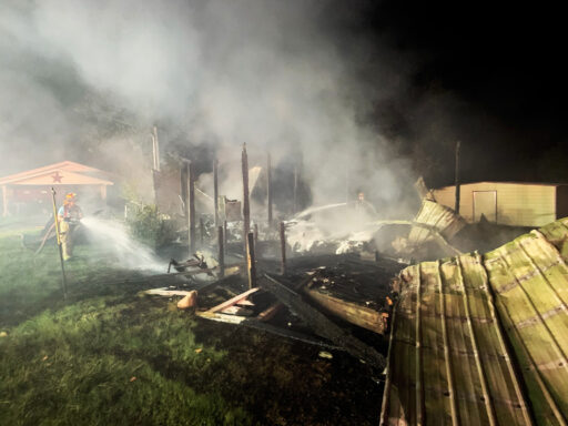 Large metal debris with smoke coming off of it and a firefighter spraying a water hose on the smoke