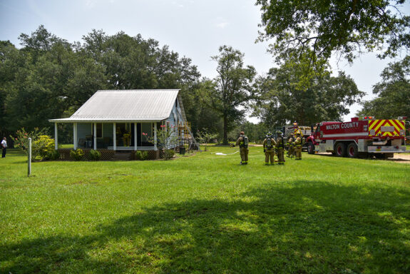 Two fire engines and several firefighters outside of small blue house with smoke damage