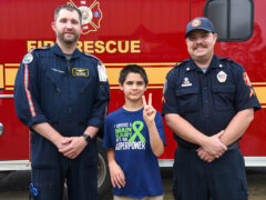 Young boy with dark brown hair holding up the peace sign next to a flight paramedic and a paramedic