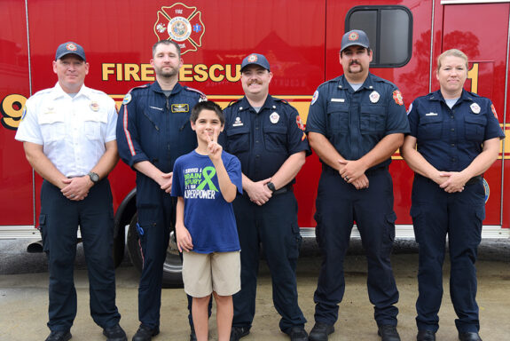 Young boy with dark brown hair standing with four EMTs and paramedics