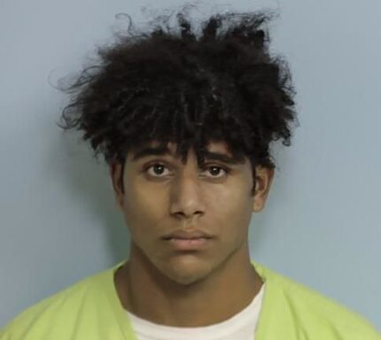 A mug shot of a black teenager wearing a lime green jumpsuit with curly hair.