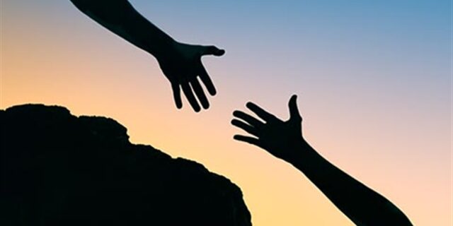 Two hands reaching out for one another with a mountain ledge.