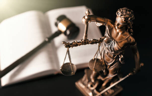Lady Justice with a gavel and a law book in the background.