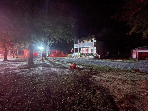 Large two story home with fire trucks and firefighters out front at night