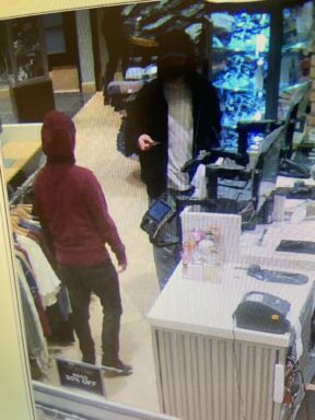 Two males standing at a cashiers counter one is wearing a maroon sweatshirt the other is wearing a black zip-up hoodie.