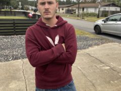 A white male with his arms crossed wearing a maroon sweatshirt and jeans.