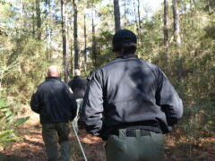 A black female and a white male with a shaved head walk along a path in a wooded area.