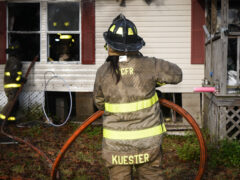 Two firefighters holding a hose line outside of single story home