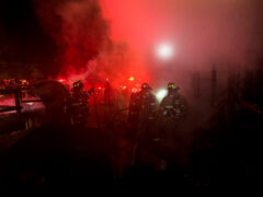 Firefighters standing in debris after knocking down a structure fire at night