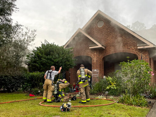 Firefighters Outside of single-story brick home with smoke coming out of the roof