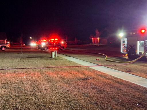 Fire trucks with flashing red lights lining a roadway in a residential neighborhood