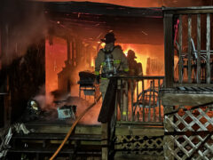 Firefighters fighting a fire inside the front door of a burning double wide mobile home