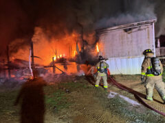 Firefighters outside of a double wide mobile home fire at night