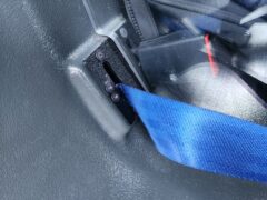 A blue seat belt built into the plastic rear seat of a patrol car.