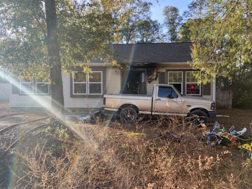 Single story home with smoke damage around front door with a gold truck parked in front