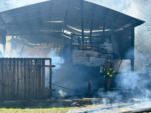 Firefighters fighting a fire in a camper parked underneath a large metal barn
