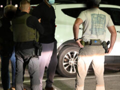 A tall black male being put in handcuffs by three uncover deputies.