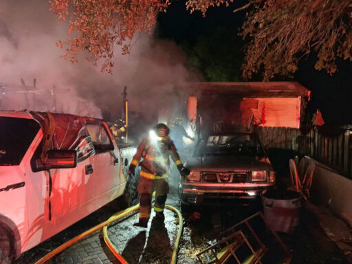 Firefighter walking next to a yellow fire hose line outside of a home at night