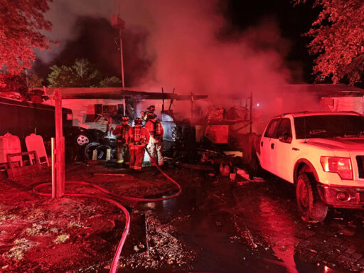 Firefighters outside of single-wide mobile home with smoke coming from it at night